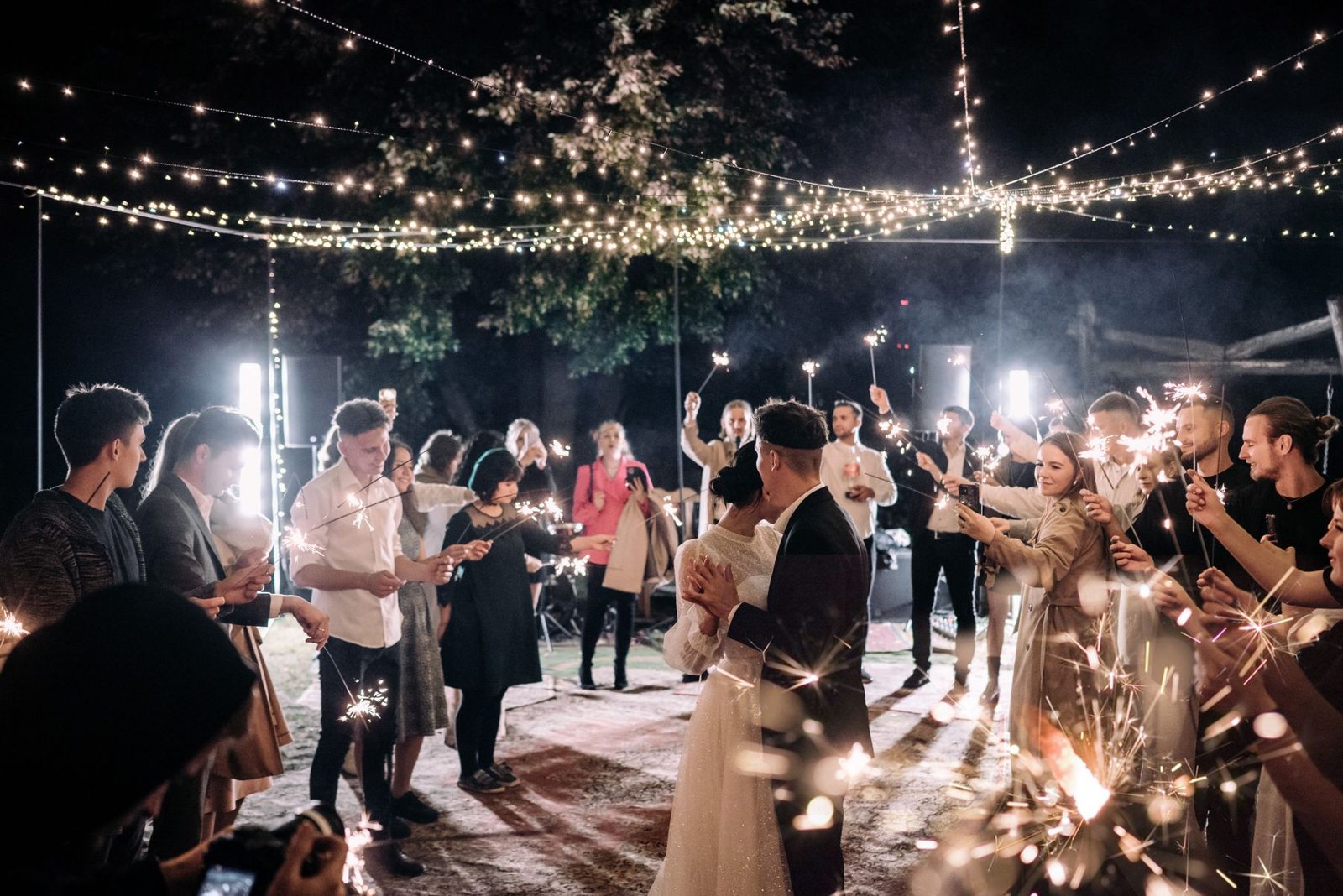 A wedding couple dancing with guests and sparklers around them